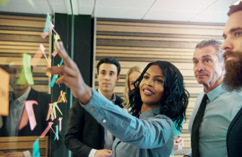 Photo of a businesswoman using organization skills to lay out a plan for her coworkers on a wall of sticky notes.